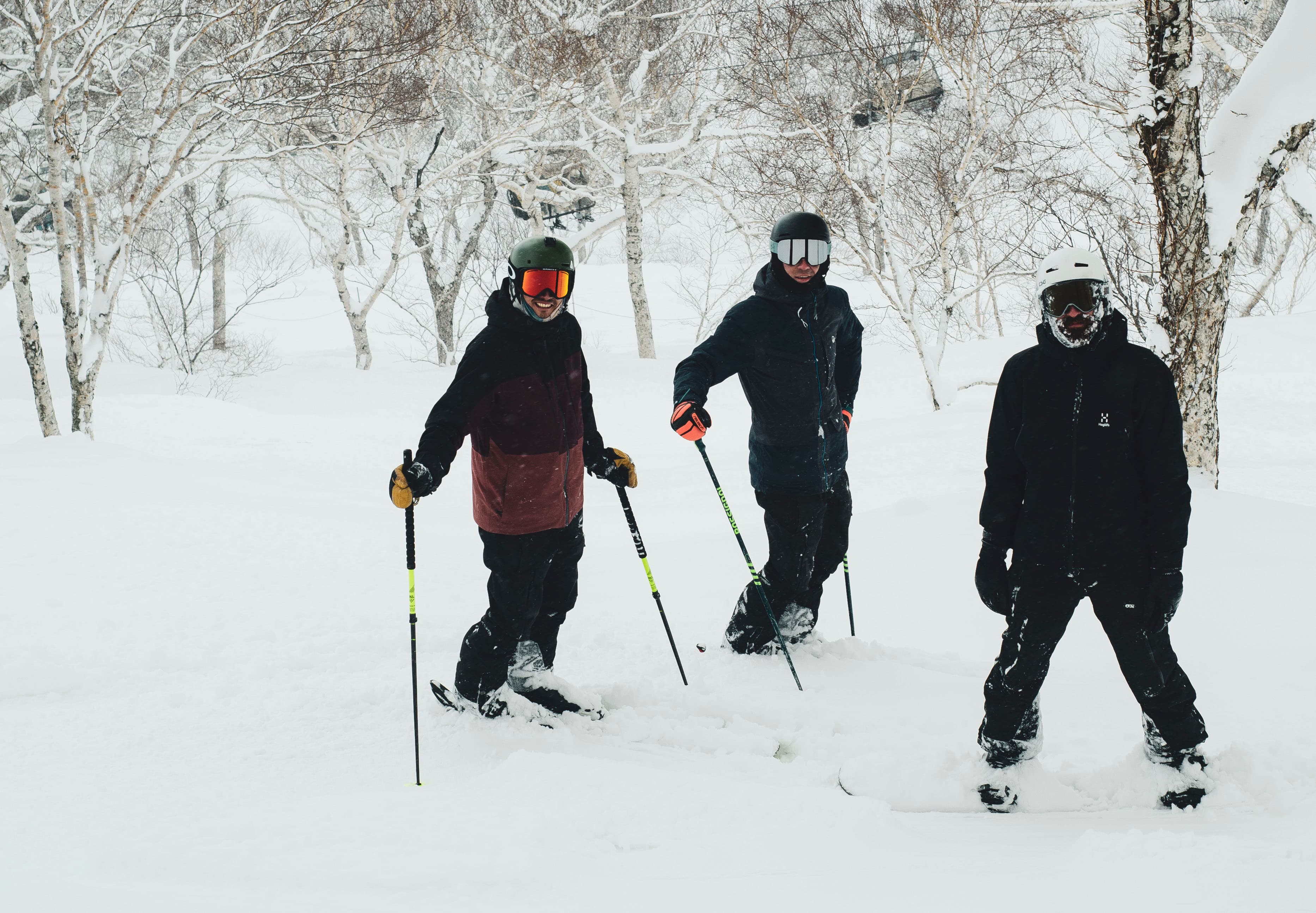 Two skiers and a snowboarder pose in a snowy forest wearing helmets and goggles.