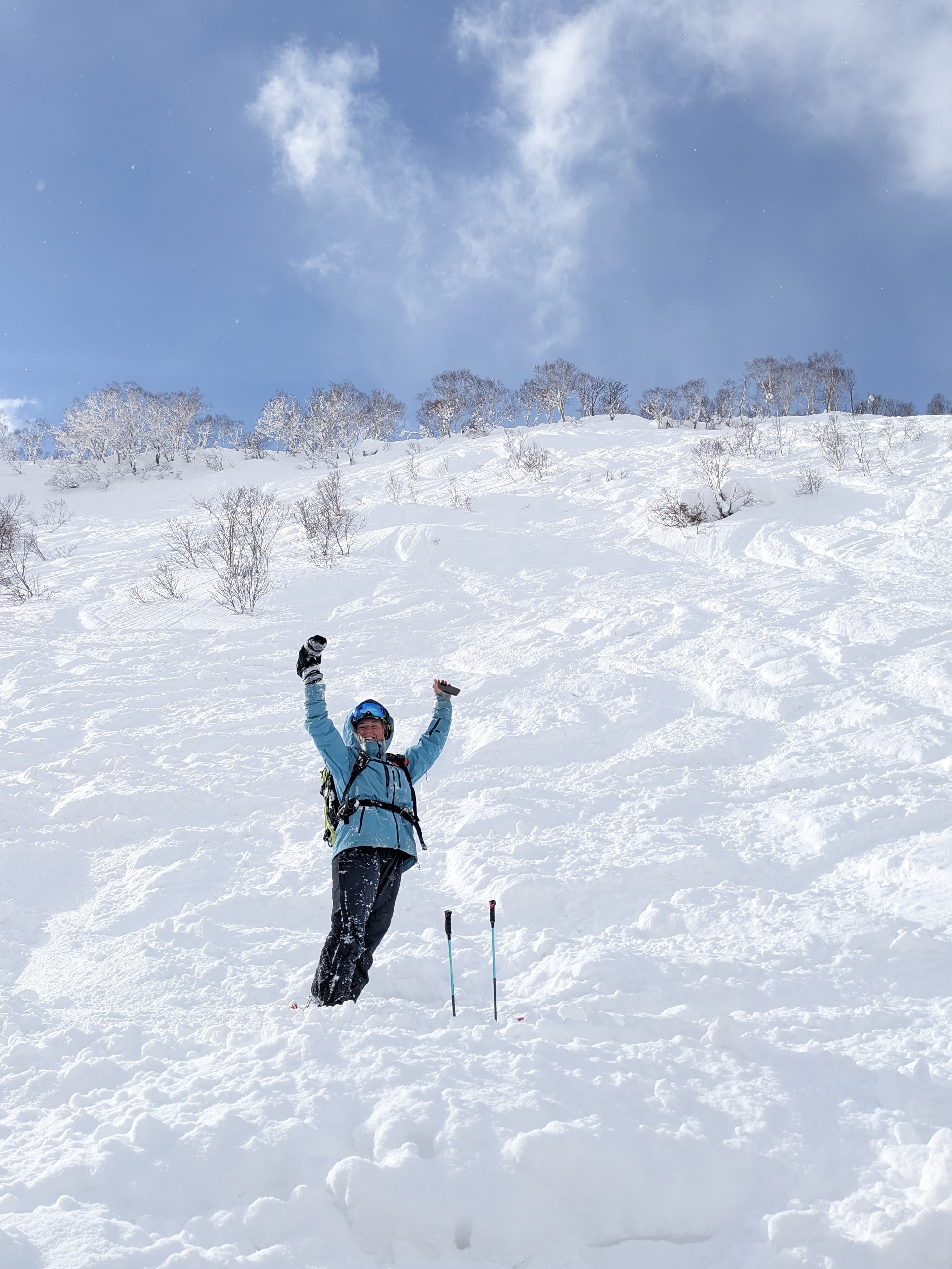 Skier in blue jacket celebrates with arms raised on a steep, snow-covered mountain slope.