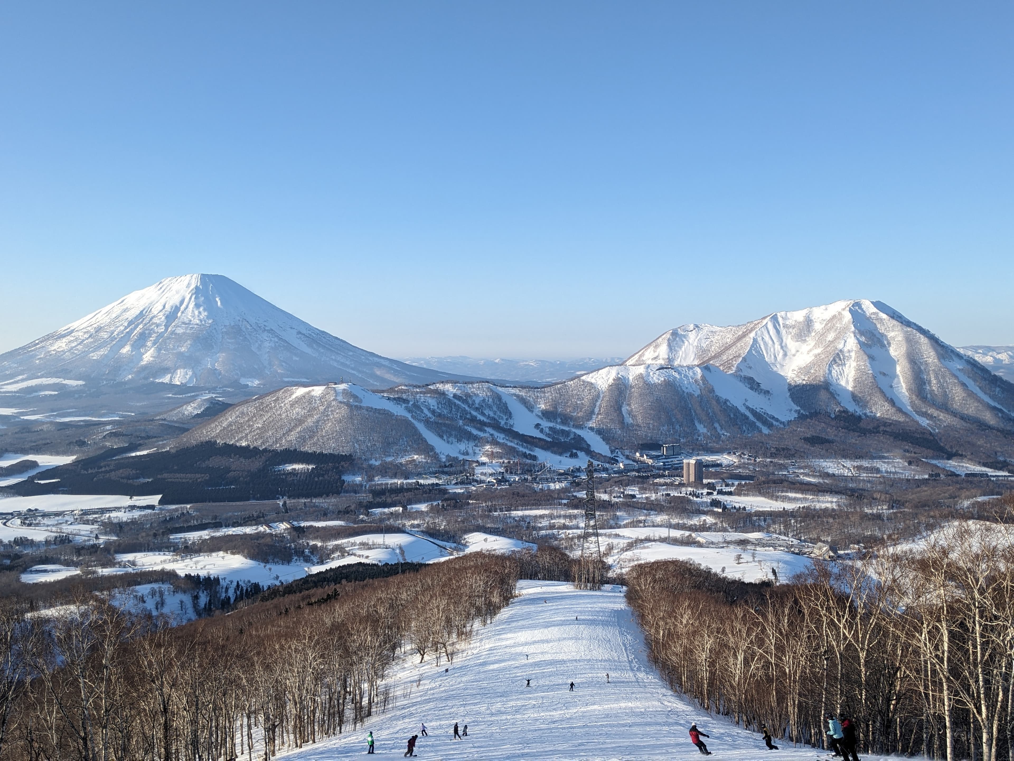 Skiers descend a snowy slope with a panoramic view of two majestic snow-capped mountains.