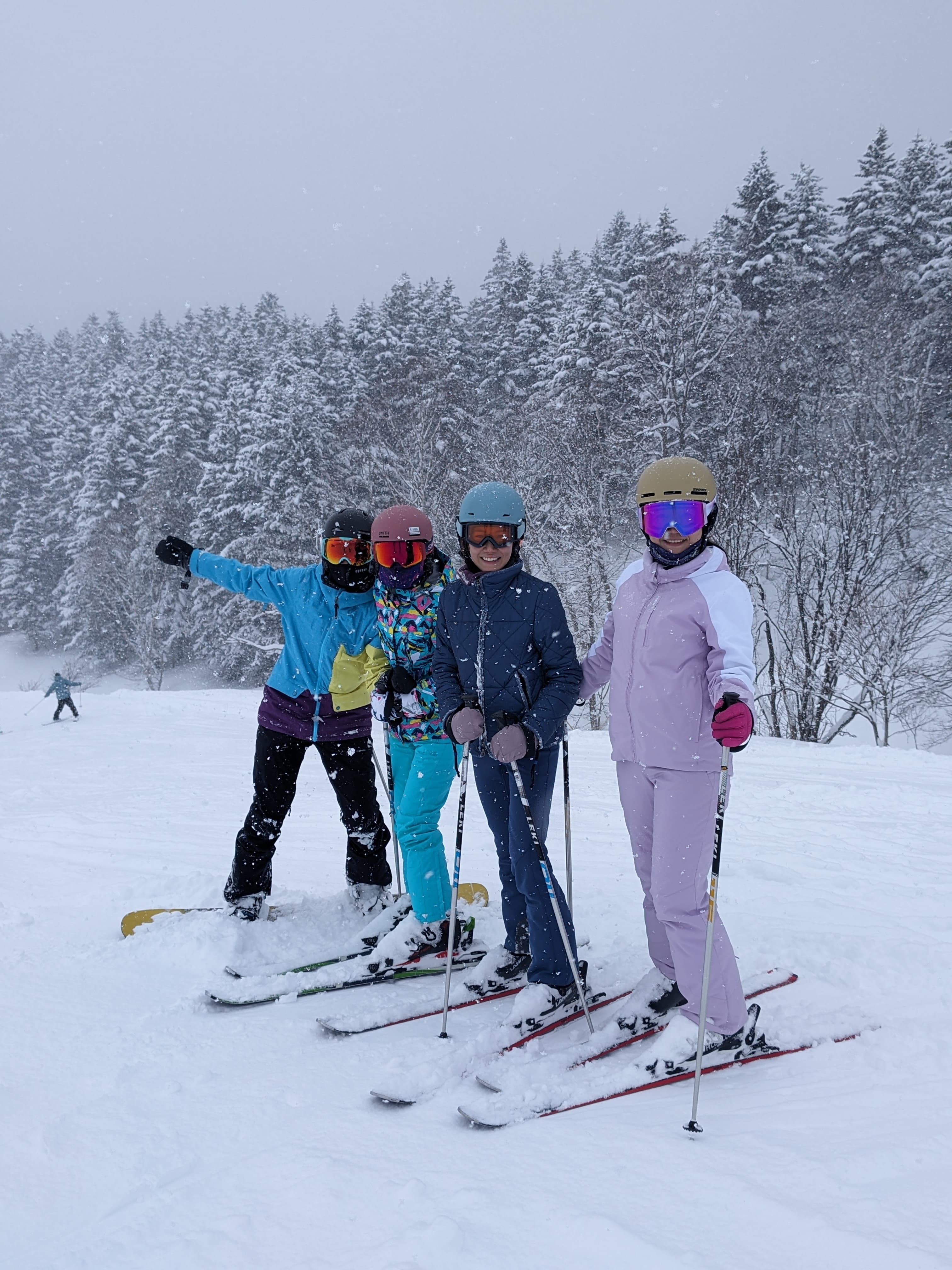 Four people in winter gear posing on a snowy slope with skis and snowboard.