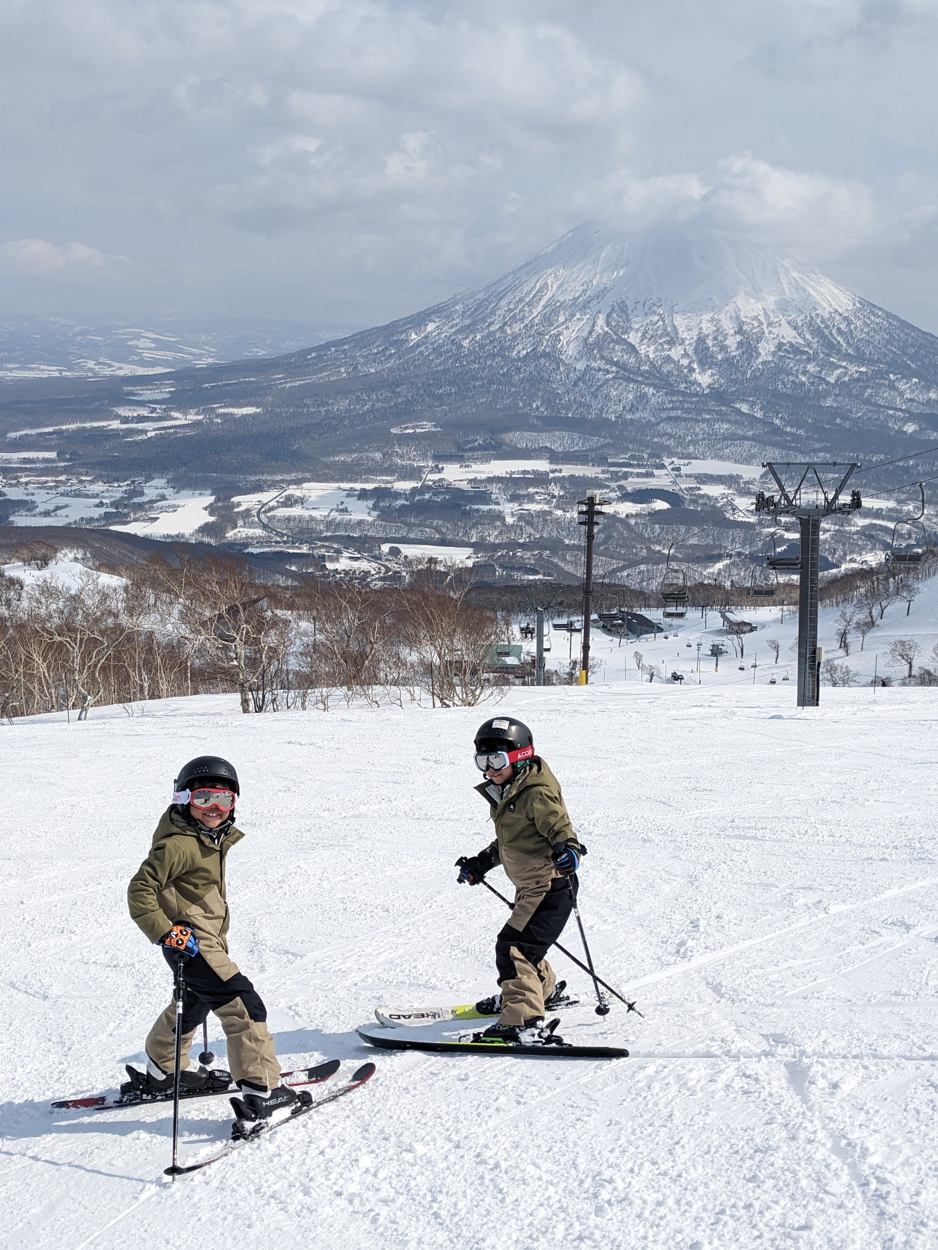 Two young skiers on a snowy slope with a massive snow-covered mountain in the distance.