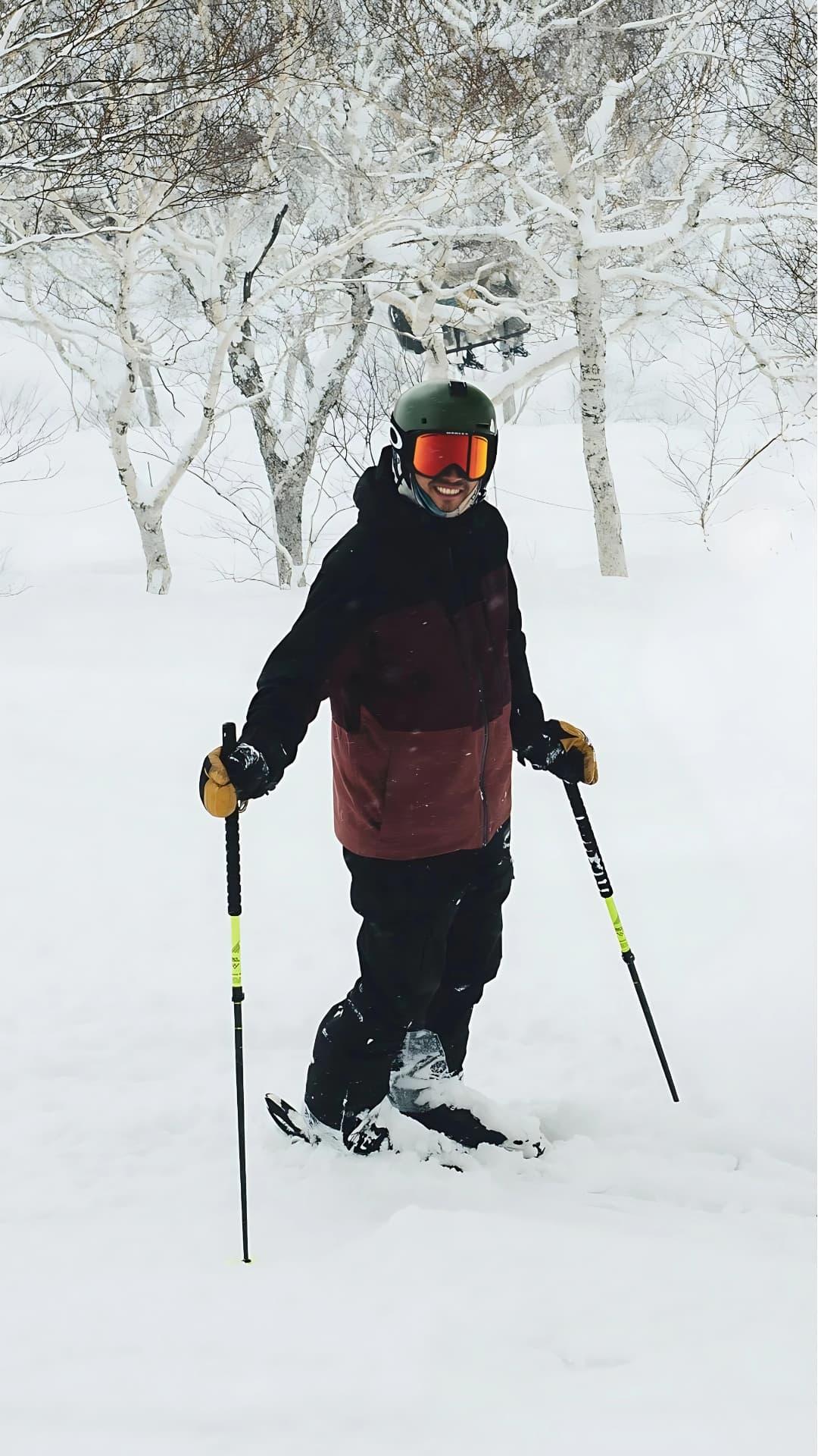 Smiling skier in winter gear stands in a snowy forest with frost-covered trees.